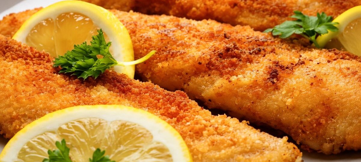 Filés de peixe empanados fritos dourados servidos em prato branco com limão siciliano e salsa fresca