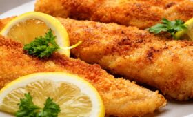 Filés de peixe empanados fritos dourados servidos em prato branco com limão siciliano e salsa fresca