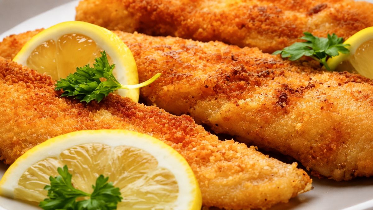 Filés de peixe empanados fritos dourados servidos em prato branco com limão siciliano e salsa fresca