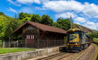 Estação Ferroviária Neri Ferreira em Mendes, Rio de Janeiro, com prédio de madeira histórico e locomotiva azul da MRS passando nos trilhos.