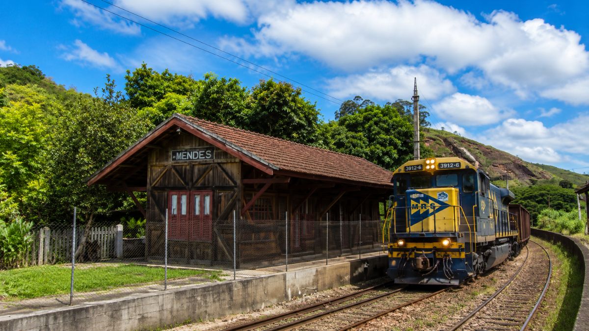 Estação Ferroviária Neri Ferreira em Mendes, Rio de Janeiro, com prédio de madeira histórico e locomotiva azul da MRS passando nos trilhos.