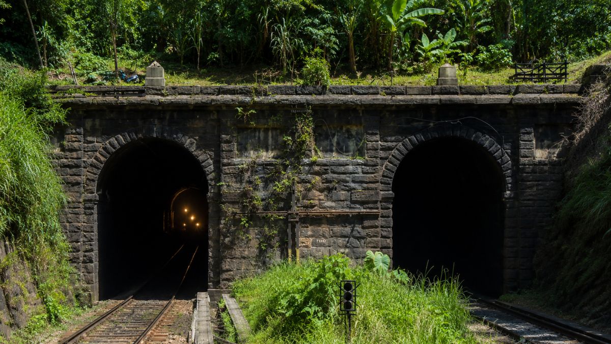 Entrada dupla em arco de pedra do histórico Túnel 12 exibindo trilhos ferroviários e luzes internas no município de Mendes.