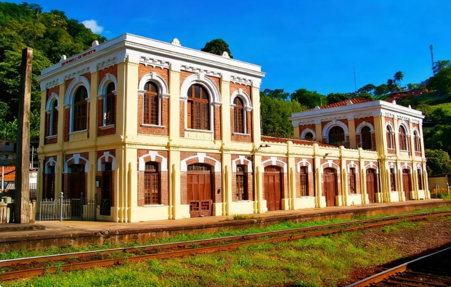 Fachada da histórica estação de trem de Engenheiro Paulo de Frontin, com sua arquitetura em tons de amarelo e tijolo aparente, sob um céu azul e cercada por vegetação.