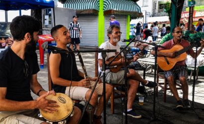 Quatro músicos tocam instrumentos como pandeiro, clarinete, cavaquinho e violão ao ar livre na Praça Doutor João Neri em Mendes.