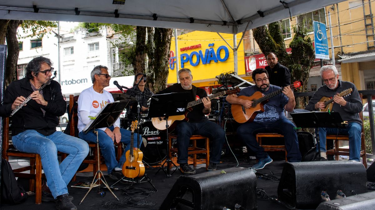 Conjunto de músicos sentados tocando flauta violão e cavaquinho sob tenda na Praça Dr Joao Neri em Mendes.