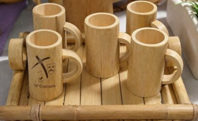 Conjunto de canecas feitas de bambu com alças circulares organizadas sobre uma bandeja de hastes de bambu em superfície clara.