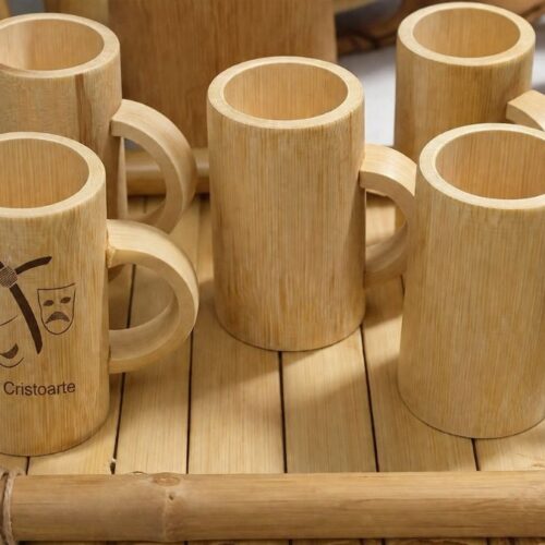 Conjunto de canecas feitas de bambu com alças circulares organizadas sobre uma bandeja de hastes de bambu em superfície clara.
