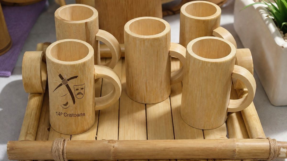 Conjunto de canecas feitas de bambu com alças circulares organizadas sobre uma bandeja de hastes de bambu em superfície clara.