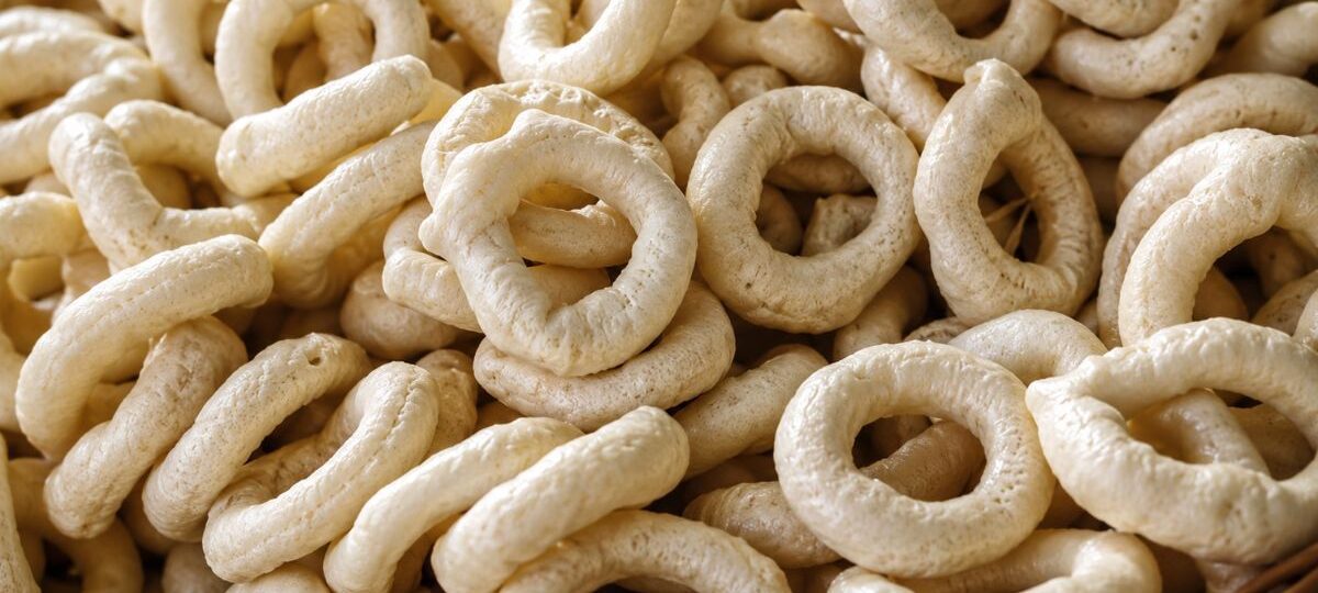 Uma pilha de biscoitos de polvilho azedo artesanais em formato de rosquinha com textura porosa e cor bege claro.