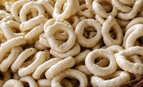 Uma pilha de biscoitos de polvilho azedo artesanais em formato de rosquinha com textura porosa e cor bege claro.