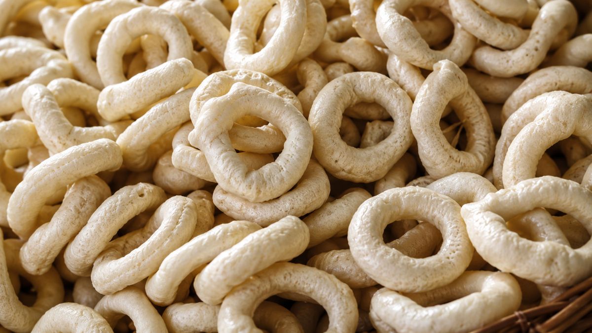 Uma pilha de biscoitos de polvilho azedo artesanais em formato de rosquinha com textura porosa e cor bege claro.
