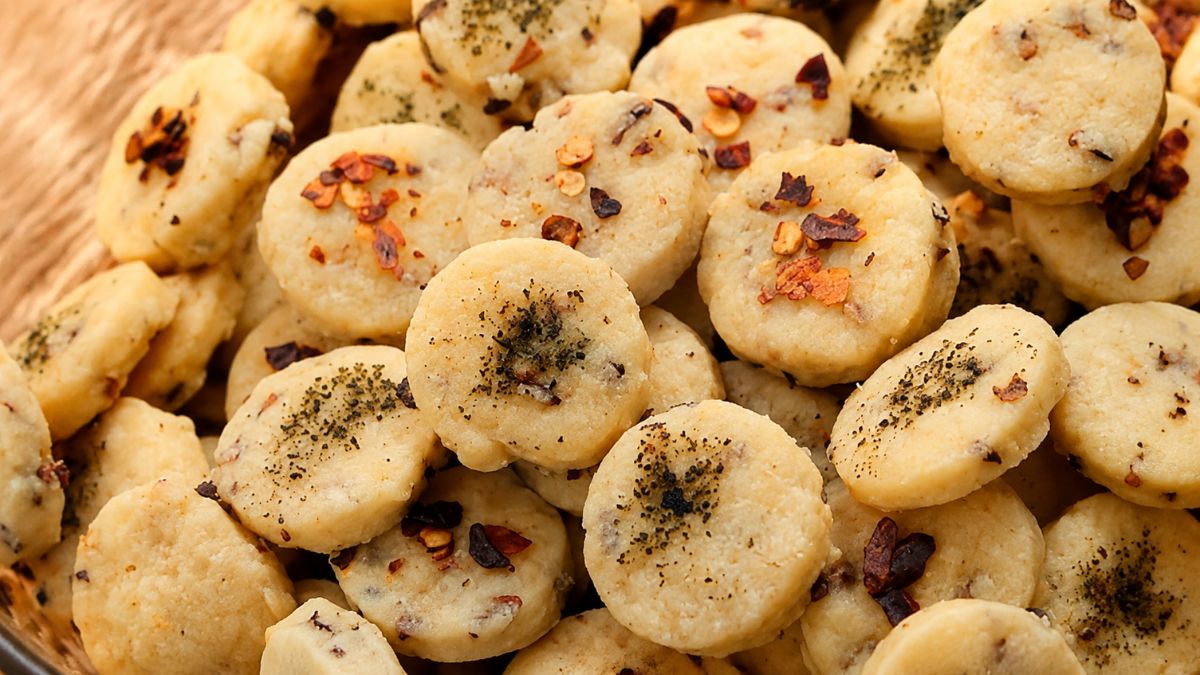 Biscoitos salgados caseiros amanteigados em formato redondo, polvilhados com ervas e pimenta em flocos, dispostos em uma cesta.