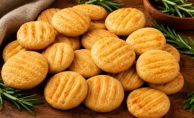 Biscoitos de cebola caseiros e crocantes marcados com garfo, dispostos em uma tábua de madeira rustica decorada com ramos de alecrim fresco.
