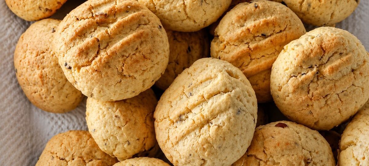 Uma pilha de biscoitos caseiros redondos e dourados com marcas de garfo na superfície e pedaços visíveis de castanha do pará.