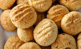 Uma pilha de biscoitos caseiros redondos e dourados com marcas de garfo na superfície e pedaços visíveis de castanha do pará.