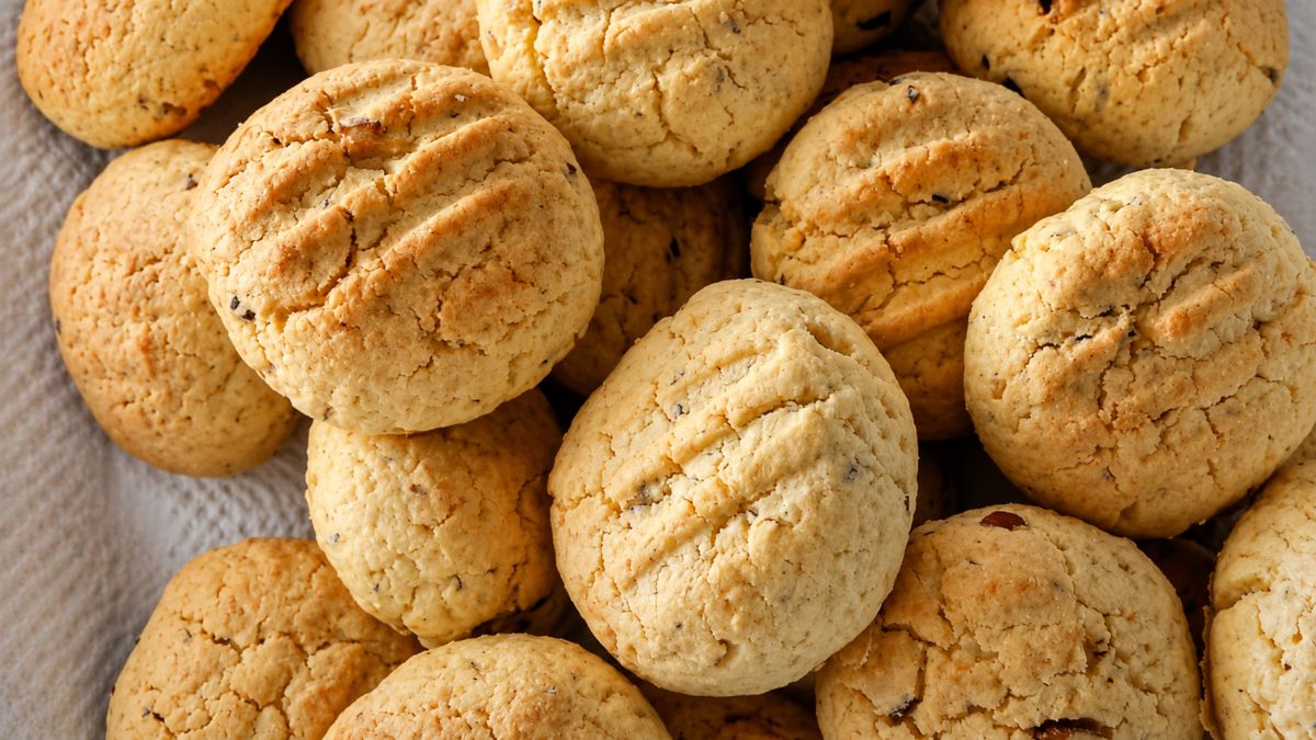 Uma pilha de biscoitos caseiros redondos e dourados com marcas de garfo na superfície e pedaços visíveis de castanha do pará.
