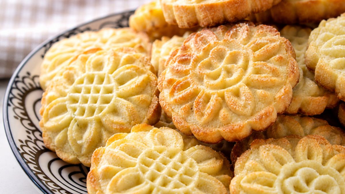 Close-up de uma pilha de biscoitos amanteigados caseiros com desenhos de flores douradas em um prato de cerâmica preta e branca.