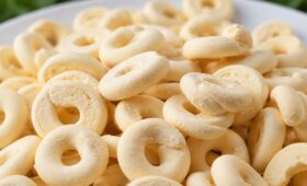 Um close em uma pilha de biscoitos de polvilho e leite condensado amarelos claros, em formato de rosca, em um prato branco.