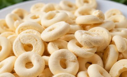 Um close em uma pilha de biscoitos de polvilho e leite condensado amarelos claros, em formato de rosca, em um prato branco.