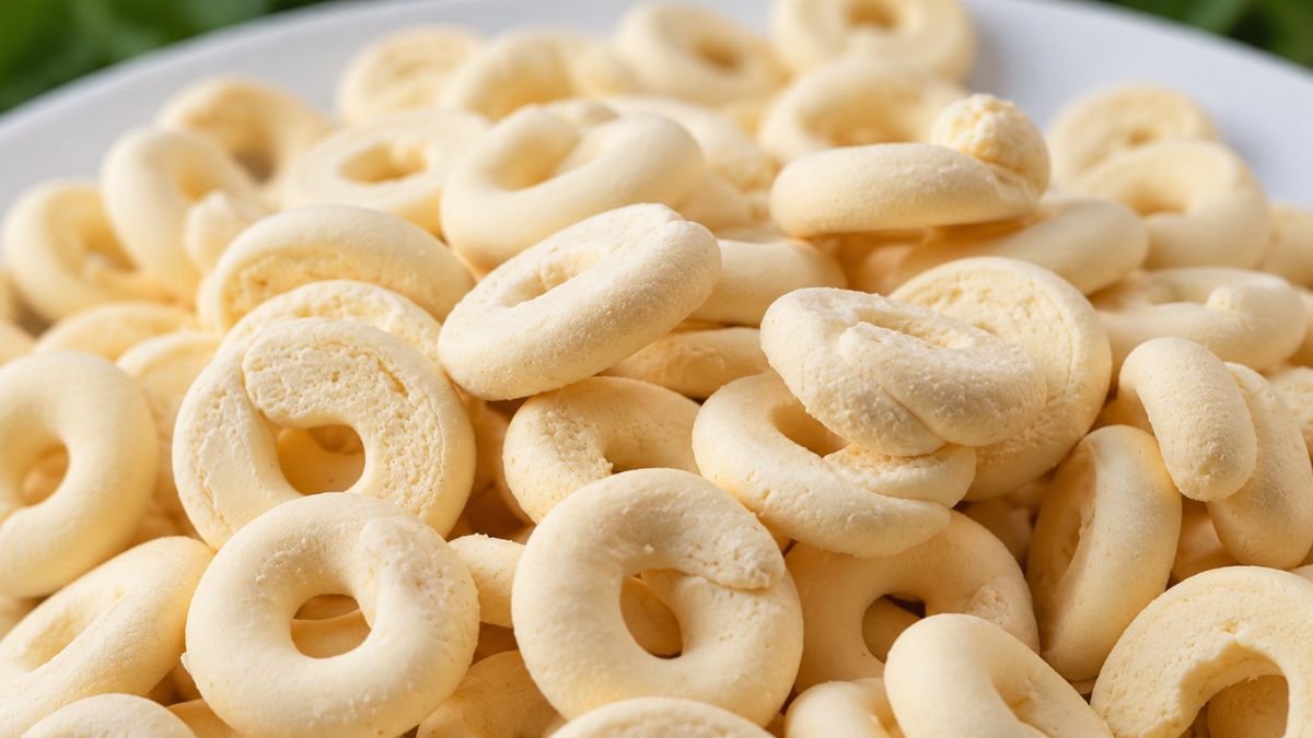 Um close em uma pilha de biscoitos de polvilho e leite condensado amarelos claros, em formato de rosca, em um prato branco.