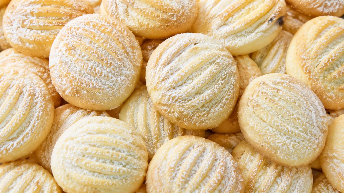 Close-up em plano superior de diversos biscoitos de baunilha redondos, com textura listrada e polvilhados com açúcar de confeiteiro, organizados em uma pilha.