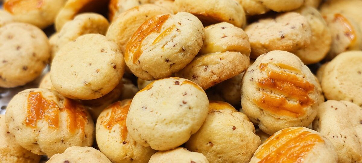 Pilha de pequenos biscoitos artesanais dourados com queijo ralado visível na massa e uma calda de queijo derretido por cima.