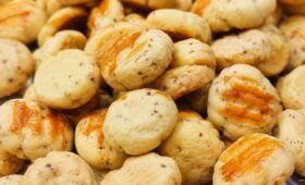 Pilha de pequenos biscoitos artesanais dourados com queijo ralado visível na massa e uma calda de queijo derretido por cima.