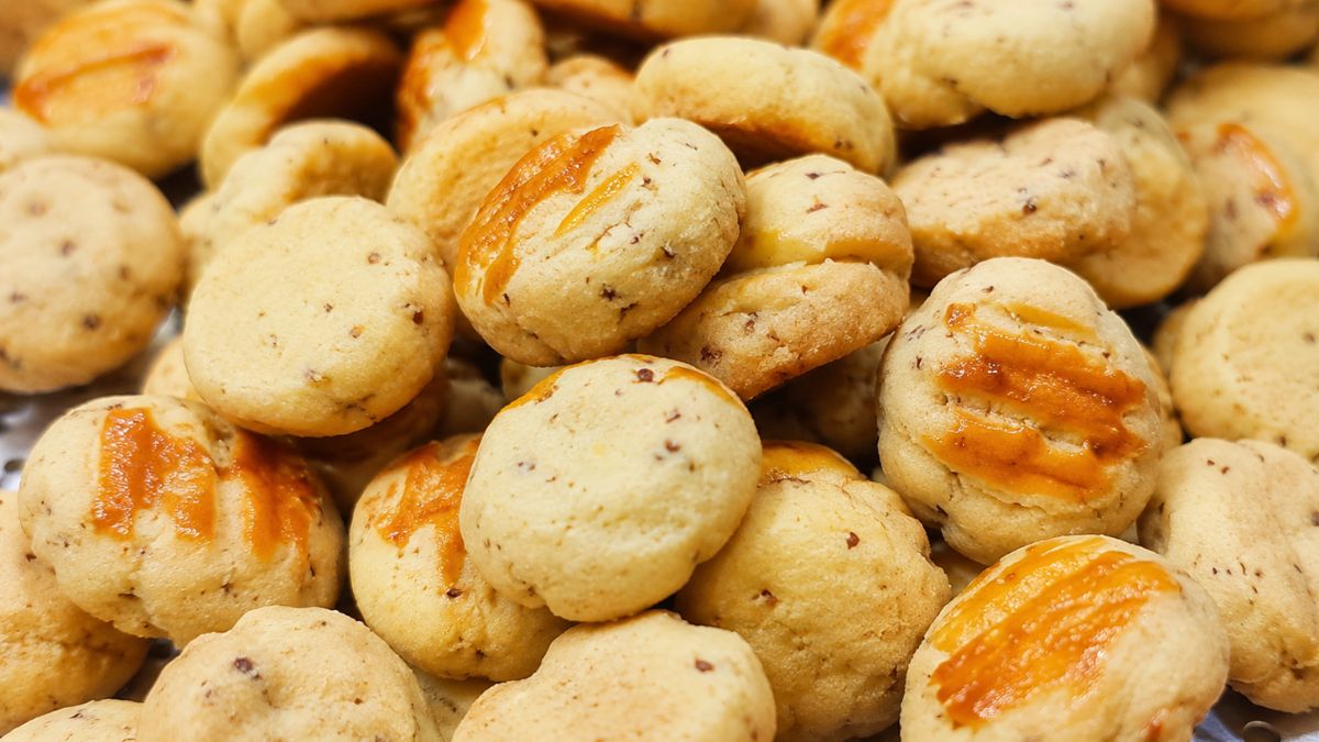 Pilha de pequenos biscoitos artesanais dourados com queijo ralado visível na massa e uma calda de queijo derretido por cima.