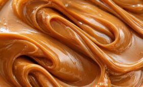 Close-up texturizado de doce de leite caseiro super cremoso e brilhante, mostrando as ondas suaves e a cor caramelo dourado de uma textura aveludada perfeita.