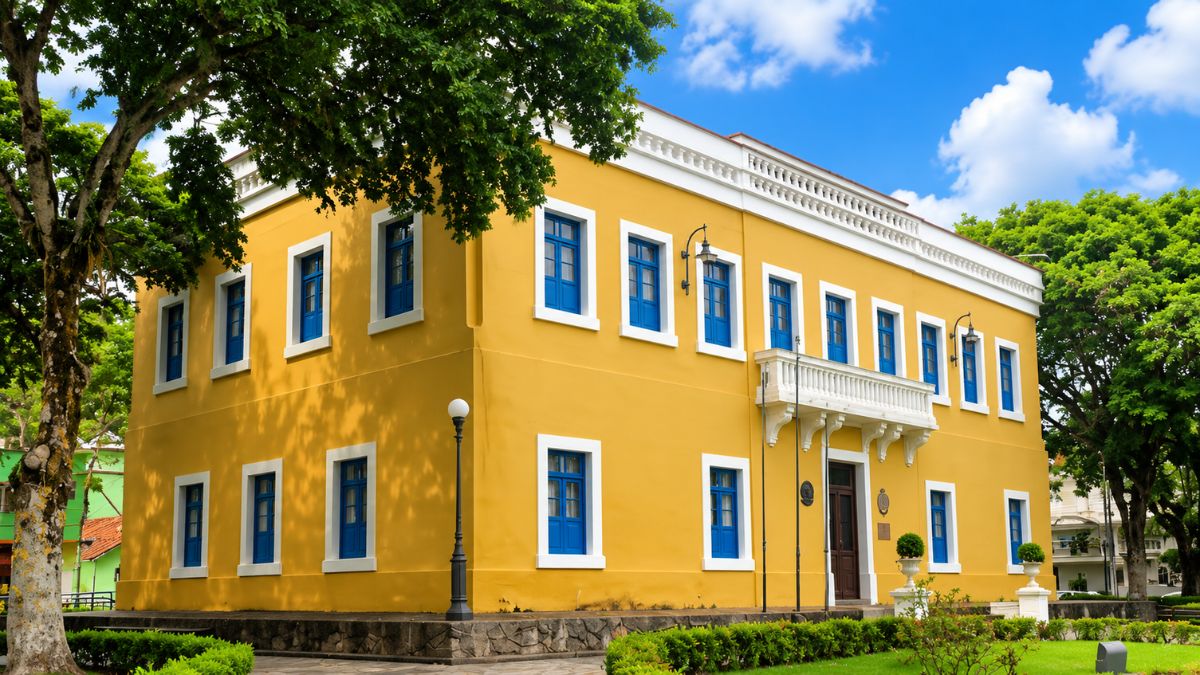 Fotografia do Palácio Imperial em Piraí, exibindo um casarão histórico de dois pavimentos pintado de amarelo com janelas azuis, molduras brancas e sacada central sob céu azul.