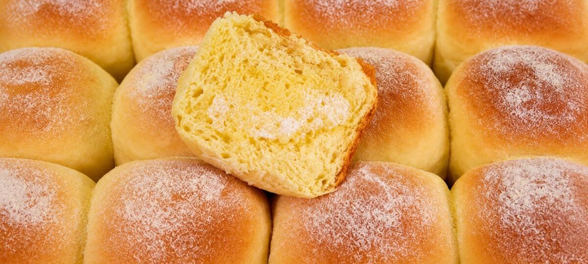 Pães de milho dourados em fileiras na assadeira com açúcar polvilhado por cima e uma fatia cortada mostrando o miolo amarelo macio e aerado.