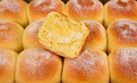 Pães de milho dourados em fileiras na assadeira com açúcar polvilhado por cima e uma fatia cortada mostrando o miolo amarelo macio e aerado.