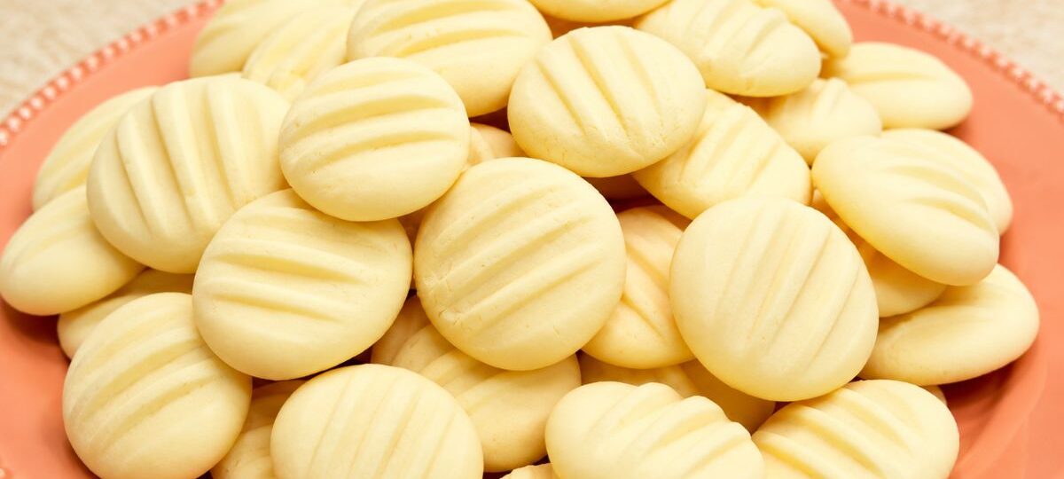 Biscoitos de amido de milho caseiros redondos e claros com marcas de garfo empilhados em um prato de cerâmica salmão.