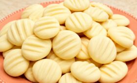 Biscoitos de amido de milho caseiros redondos e claros com marcas de garfo empilhados em um prato de cerâmica salmão.
