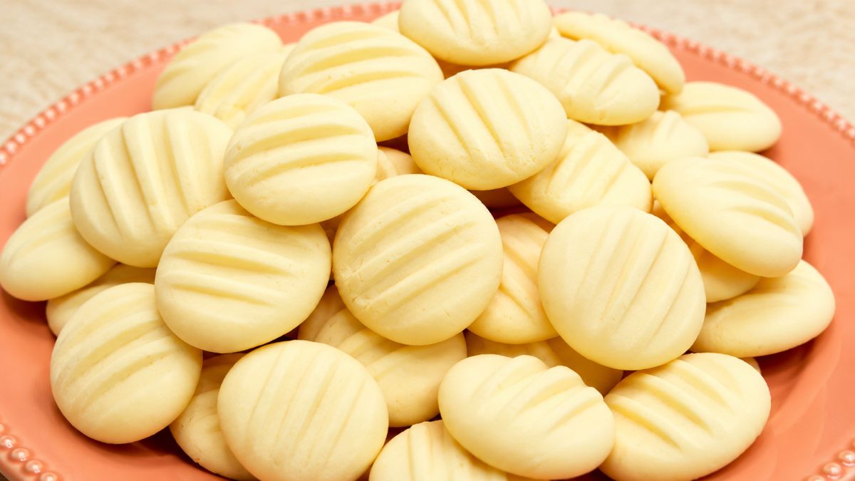 Biscoitos de amido de milho caseiros redondos e claros com marcas de garfo empilhados em um prato de cerâmica salmão.