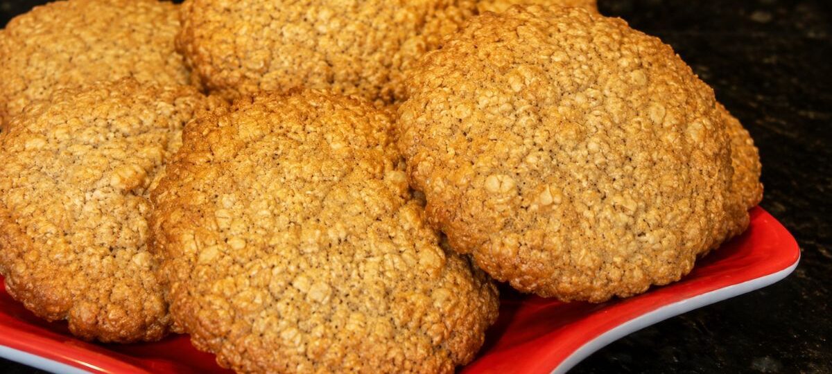 Foto em close de diversos biscoitos caseiros integrais dourados com textura visível de farelo e linhaça dispostos em um prato vermelho sobre uma bancada preta.