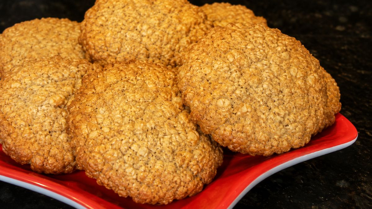 Foto em close de diversos biscoitos caseiros integrais dourados com textura visível de farelo e linhaça dispostos em um prato vermelho sobre uma bancada preta.