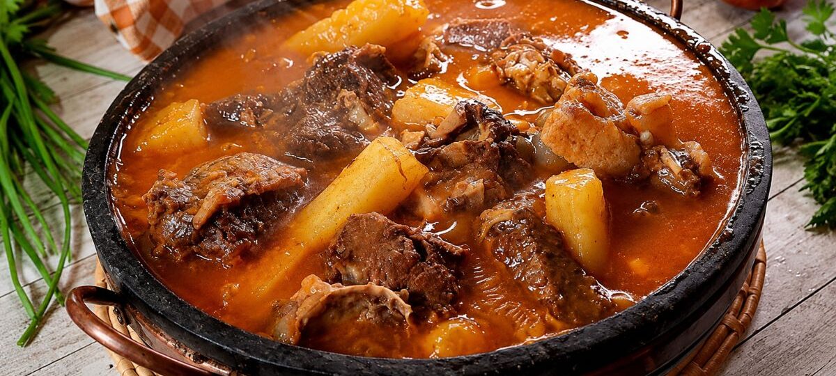Panela de pedra rústica servindo vaca atolada da roça quente com pedaços suculentos de costela bovina e mandioca cozida em caldo cremoso.