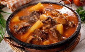 Panela de pedra rústica servindo vaca atolada da roça quente com pedaços suculentos de costela bovina e mandioca cozida em caldo cremoso.