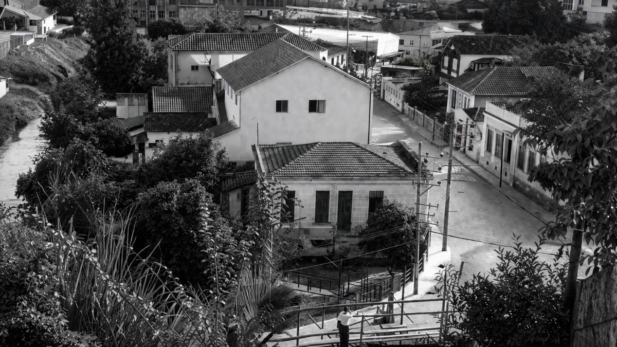 Fotografia aérea em preto e branco mostrando o centro histórico de Mendes, RJ, com casarões antigos, ruas pavimentadas, vegetação e postes.